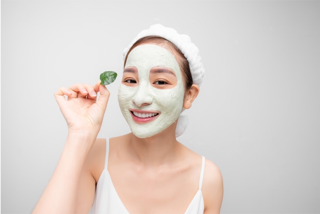 Mulher sorridente com máscara facial hidratante, destacando a importância de manter a pele saudável para prevenir foliculite.