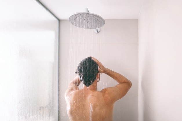 Homem de costas tomando banho de chuveiro, ilustrando o uso do sabonete íntimo masculino para a higiene do homem.