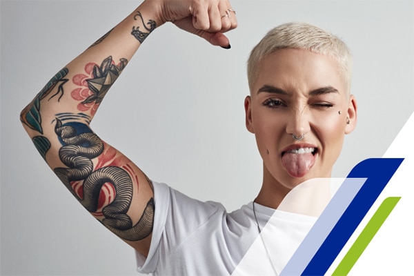 Mulher com o braço tatuado levantado piscando o olho e com a língua de fora