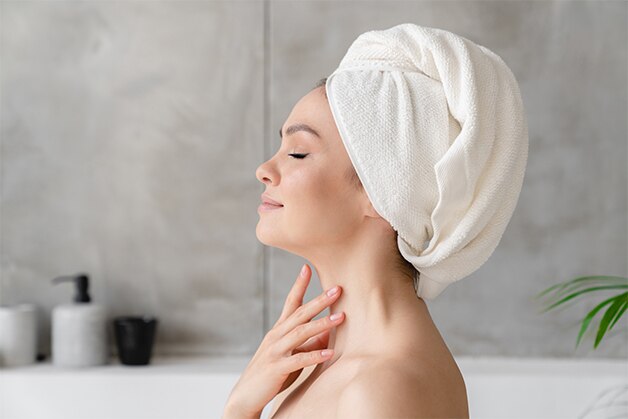 Mulher com toalha na cabeça após tomar banho com melhor sabonete para pele mista.