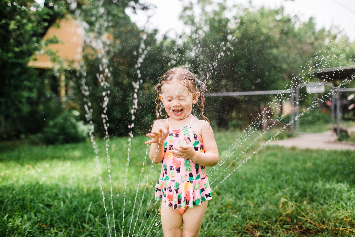 Menina se divertindo com um banho de mangueira em espaço gramado ao ar livre
