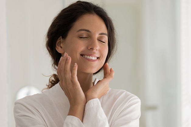 Mulher tocando o rosto durante a rotina de skincare, após passar produto com ácido salicílico para cuidar da pele.