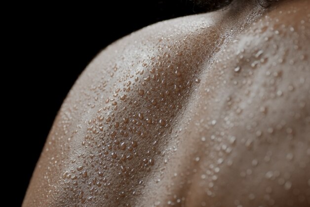 Close-up da pele de ombro e costas coberta por gotas de suor, ilustrando sinais de hiperidrose (sudorese excessiva).