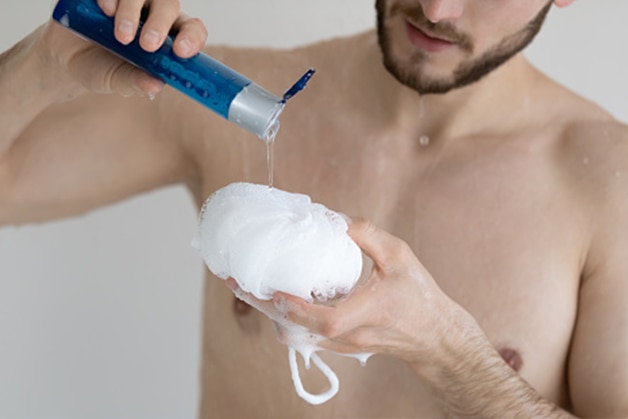 Homem colocando sabonete líquido masculino na esponja para tomar banho