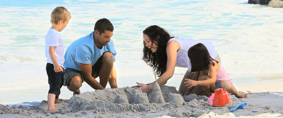 Um homem e uma mulher brincando na areia com duas crianças e fazendo castelinhos de areia