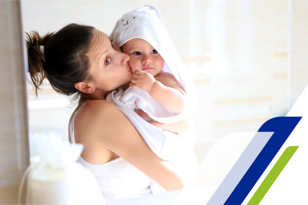 Mãe beijando o bebe que está em seu colo de toalha branca após lavar as mãos