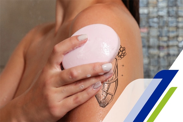 Mulher no chuveiro passando sabonete sobre a sua tatuagem no braço