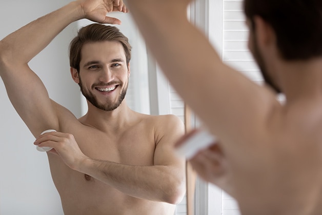 Homem em frente ao espelho passando um desodorante antibacteriano para prevenir o cheiro desagradável de suor Homem em frente ao espelho passando um desodorante antibacteriano para prevenir o cheiro desagradável de suor