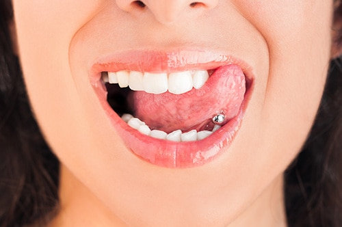 Pessoa mostrando a joia na língua para representar os cuidados com o piercing Pessoa mostrando a joia na língua para representar os cuidados com o piercing