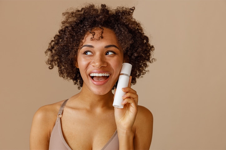 Mulher feliz e com a pele bonita segurando um frasco de produto com retinol