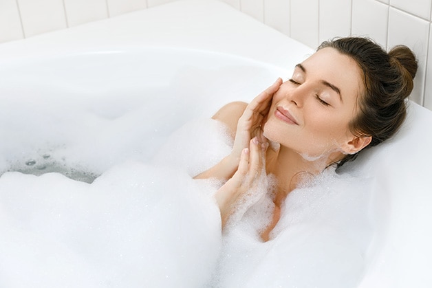 Mulher relaxando em uma banheira cheia de espuma, com os olhos fechados e um sorriso suave, aproveitando um momento de autocuidado com sabonete hidratante Mulher relaxando em uma banheira cheia de espuma, com os olhos fechados e um sorriso suave, aproveitando um momento de autocuidado com sabonete hidratante